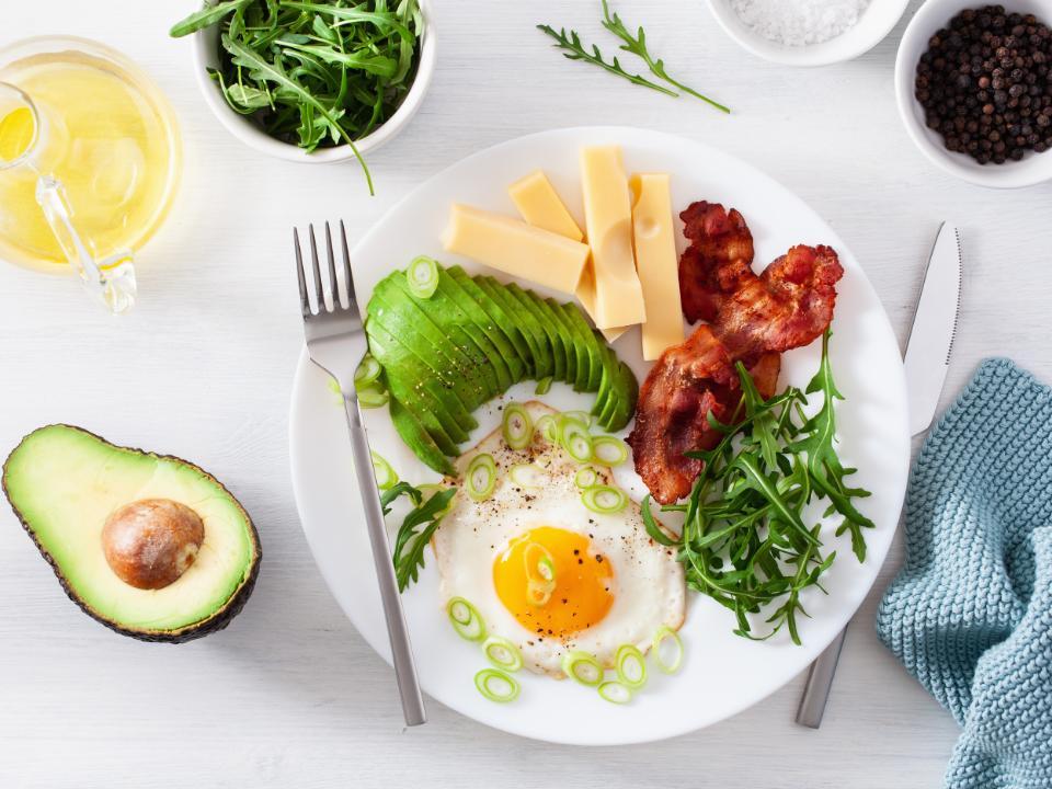 A plate of different keto foods, including avocado, eggs, bacon, cheese, and greens